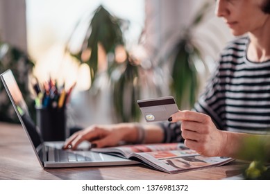 Woman Shopping Online And Using Credit Card While Reading Cosmetic Catalogue