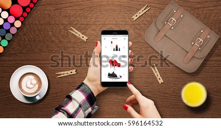 Woman shopping shoes online, holding modern phone in hands on table with bag, coffee, and makeup beside
