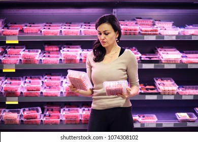 Woman Shopping In Supermarket Reading Product Information.
Chooses Meat In The Meat Department
