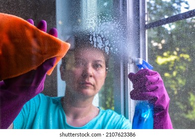 woman with short black hair in rubber gloves washes window in her apartment with rag while holding window cleaner. concept of cleaning services, window washing, housework. selective focus