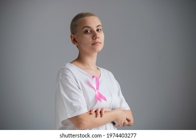 Woman with a short blonde haircut with a pink ribbon on a white t-shirt as a symbol of breast cancer on a white background.