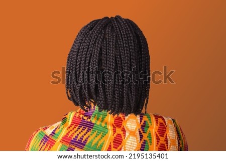 woman with short braided hair and Kente wrap on orange background