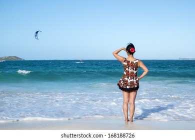 Woman in Short Floral Dress and Red Flower in Her Hair Looking Out into the Caribbean Sea - Powered by Shutterstock