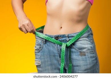 Woman with short hair in oversized jeans and measure tape isolated on yellow background. Weight loss and healthcare concept