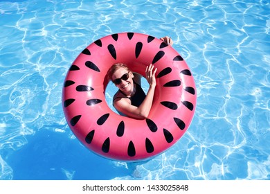 Woman With Short Hair Swimming In A Pool, Look Laughing Through Pink Floatie Inflatable Doughnut, Blue Water. Funny Mood. Space For Text Layout.                                             