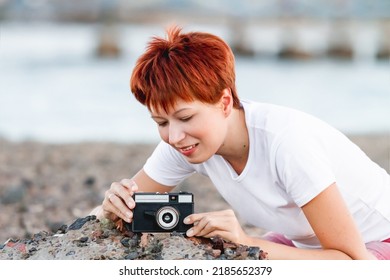 Woman With Short Red Hair Is Shooting On Vintage Film Camera. Photography As Hobby. Retro Camera With Manual Lens.