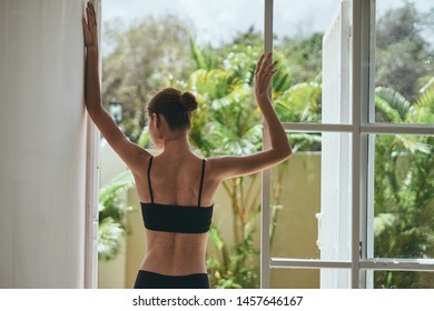 A woman in a short vest and shorts does yoga in front of a window with a room                     - Shutterstock ID 1457646167