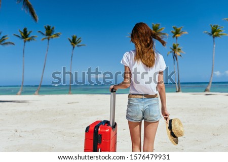 Woman in shorts and a T-shirt red suitcase sand palm trees travel                           