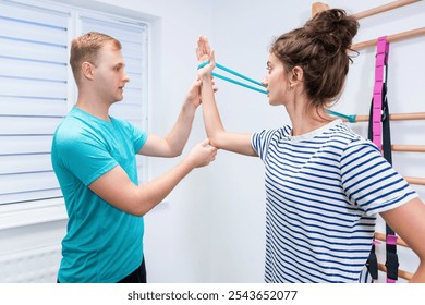 Woman with shoulder pain in physical therapy. Physical therapist exercising with female patient doing shoulder mobility exercises using resistance band. - Powered by Shutterstock