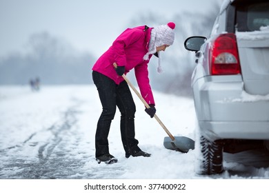 woman with a shovel removing snow around her car