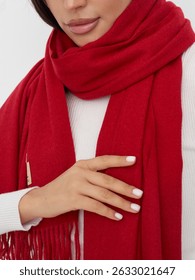 Una mujer muestra una bufanda roja vibrante, sosteniéndola suavemente contra su suéter blanco. El color brillante se destaca en la suave iluminación del espacio interior, creando un ambiente cálido.
