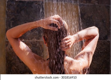 Woman in the shower, back side of young female showering under refreshing water, healthy lifestyle, enjoying time in luxury spa resort 