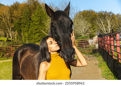 Woman showing affection to a black horse on a sunny ranch. Lifestyle. Horse riding. - Powered by Shutterstock