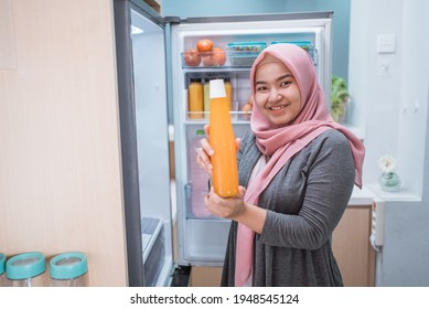 woman showing a bottle of juice in front of the fridge