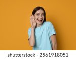 Woman showing hand to ear gesture on orange background