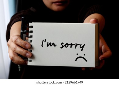 A woman showing handwritten text I'm sorry  with Sad face cartoon write on white paper.