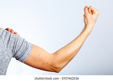 A Woman Is Showing Her Fist And Muscles Of Her Forearm And Arm In Contraction As A Gesture And Demonstration Of Strength. She Uses Her Other Hand To Roll Back The Sleeve. Concept For Girl Power.