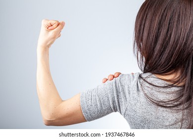 A Woman Is Showing Her Fist And Muscles Of Her Forearm And Arm In Contraction As A Gesture And Demonstration Of Strength. She Uses Her Other Hand To Roll Back The Sleeve. Concept For Girl Power.