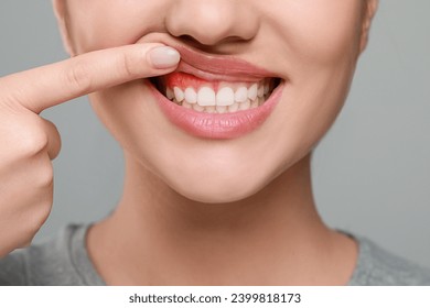Woman showing inflamed gum on grey background, closeup