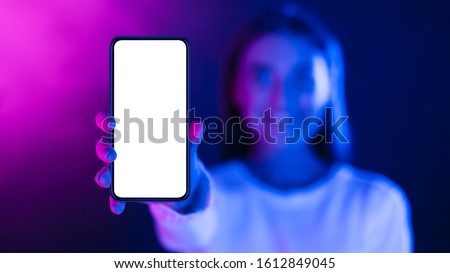 Woman showing phone with blank screen in neon lights, stretching cellphone to camera, free space