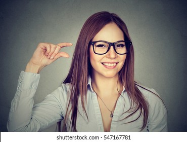 Woman Showing Small Amount Size Gesture With Hand Fingers Isolated On Gray Wall Background. Human Emotion Facial Expression Feelings Symbol