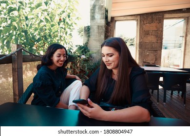 A Woman Showing Something On The Mobile Phone To Another Women While They Are Laughing