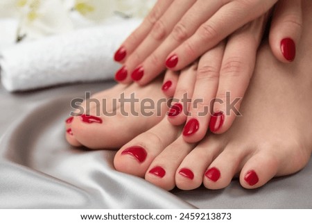 Woman showing stylish toenails after pedicure procedure and manicured hands with red polish on grey silk fabric, closeup