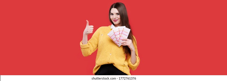 Woman showing thumb up gesture and holding lottery tickets, isolated red background