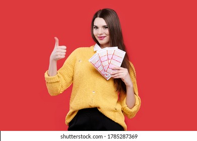 Woman showing thumb up gesture and holding lottery tickets, isolated red background