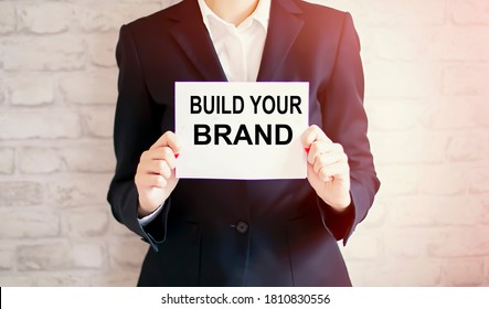 Woman Showing White Card With BUILD YOUR BRAND Word . Business Concept