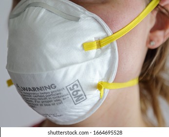 A woman is shown wearing a protective N95 white dusk mask respirator up close, set against a white background during the day.