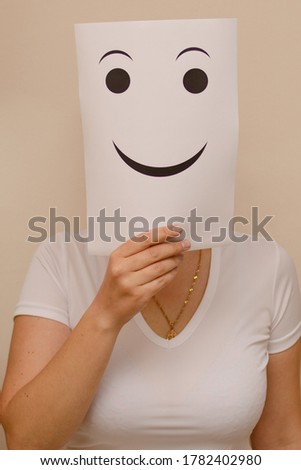 A woman shows blank sheet of paper with a smiley face in front of her face. Vertical photo, joy concept
