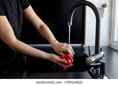 Woman shows how to wash a tomato under water in the kitchen with a black background - Powered by Shutterstock