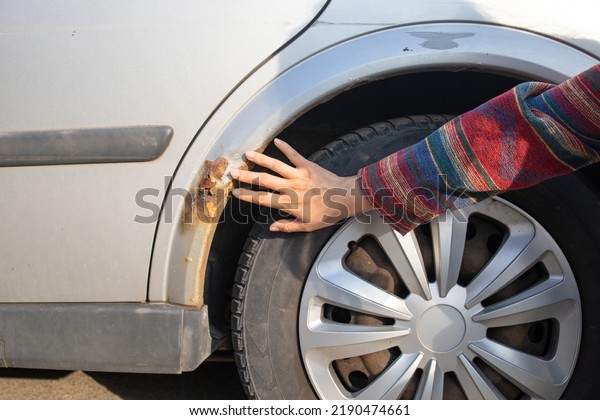A woman shows rust on a\
car door from winter reagents. Close-up, selective focus on rust\
and hand.
