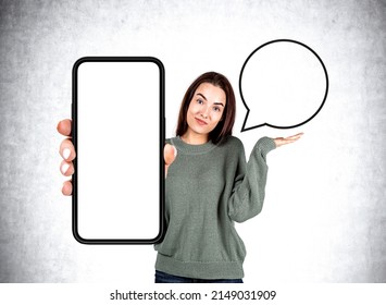 Woman shrugs hand, show phone with mockup copy space screen. Empty blank bubble speech, grey concrete wall. Concept of question and answer - Shutterstock ID 2149031909