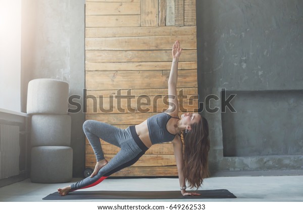 Woman in\
side plank at yoga class, Vasisthasana exercise. Fit yogi girl\
balancing on mat indoors at fitness studio\
gym