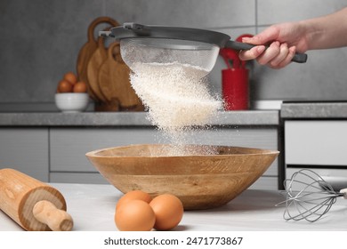 Woman sieving flour into bowl at white wooden table in kitchen, closeup - Powered by Shutterstock