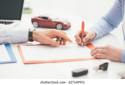 Woman signing a car insurance policy, the agent is pointing at the document