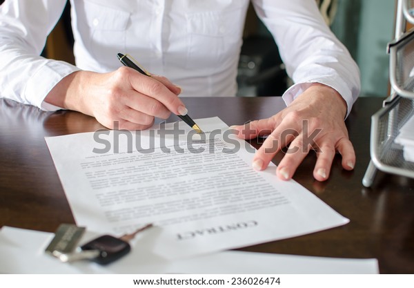 Woman\
signing a car purchase contract in car\
dealership