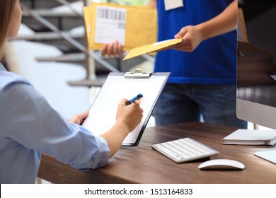 Woman signing for delivered padded envelope at table in office. Parcel shipment