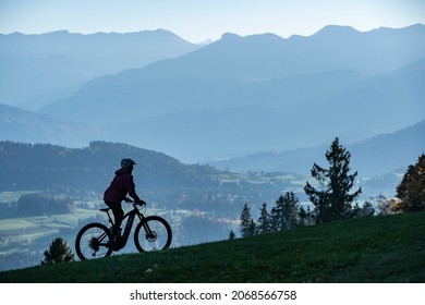 Woman as silhouette riding her electric mountain bike in the Allgaeu alps near Oberstaufen with awesome view into the Bregenz Wald Mountains, Vorarlberg , Austria - Shutterstock ID 2068566758