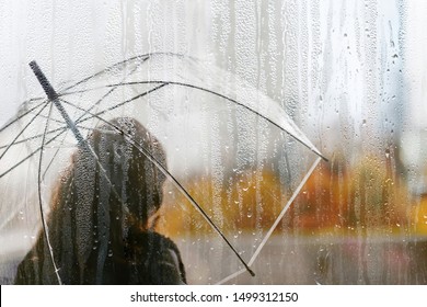 A woman silhouette with transparent umbrella through wet window with drops of rain. Autumn  - Shutterstock ID 1499312150