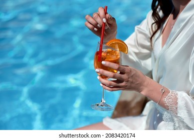 Woman in silk gown drinking aperol spritz cocktail on summer party by the pool, copy space. Event celebration concept. Traditioanal italian aperitif.