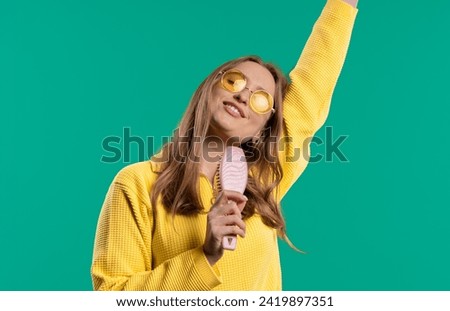 Woman singing, dancing with hair brush instead microphone on blue background. Lady having fun, listening to music, karaoke, dreams of being celebrity. High quality 