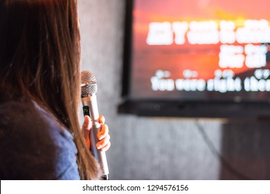 A Woman Singing At The Karaoke Bar Holding A Microphone In Front Of TV Screen With Lyrics. 