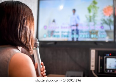 A Woman Singing A Song At The Karaoke Bar Holding A Microphone In Front Of TV Screen With Lyrics. 