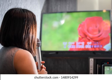 A Woman Singing A Song At The Karaoke Bar Holding A Microphone In Front Of TV Screen With Lyrics. 