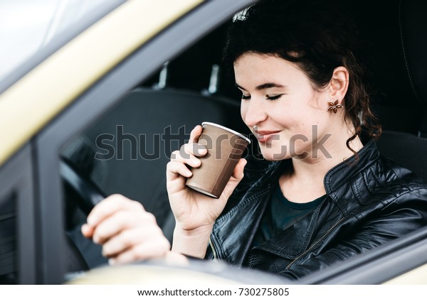 Woman sipping a\
coffee while driving a\
car.