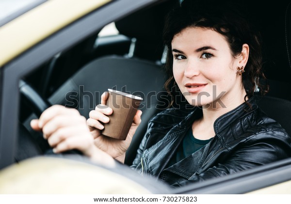 Woman sipping a\
coffee while driving a\
car.