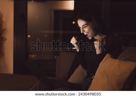 Woman sit at couch read e-mail on laptop makes yes gesture feels happy. Female entrepreneur get great business news, celebrate career growth, advance. Achievement, win, auction victory at night